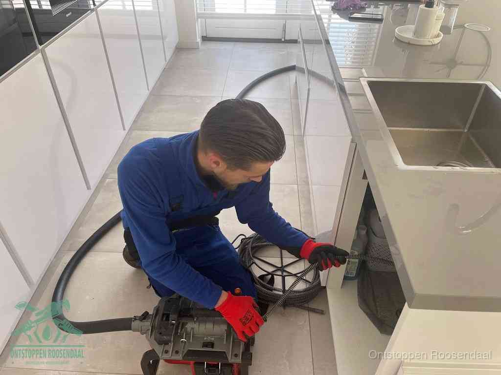 Een monteur ontstopt de keukenafvoer onder de spoelbak met een elektrische veermachine in Roosendaal