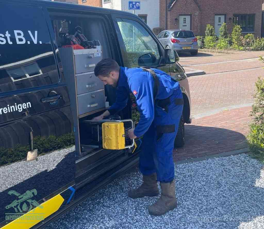 Een monteur pakt buiten op de oprit gereedschap uit de bedrijfsbus, het moment om een professional in te schakelen voor een verstopte afvoer in Roosendaal