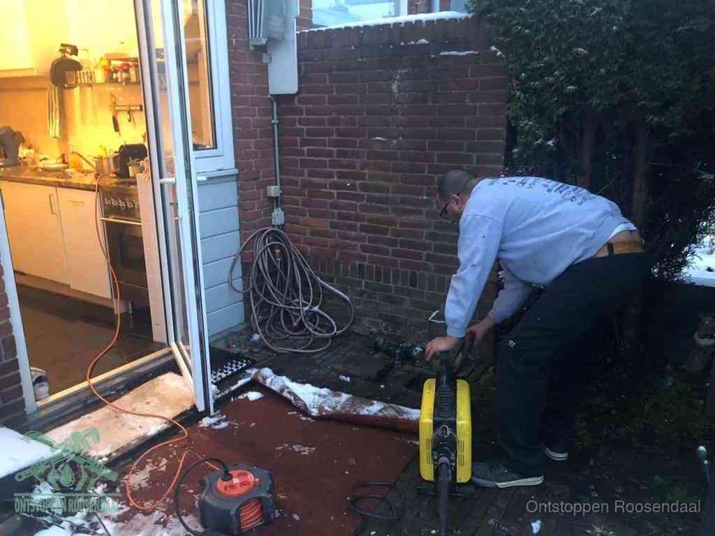 Een monteur werkt buiten bij een open riool-/grondput met een elektrische ontstoppingsmachine om een verborgen afvoerprobleem op te sporen in Roosendaal