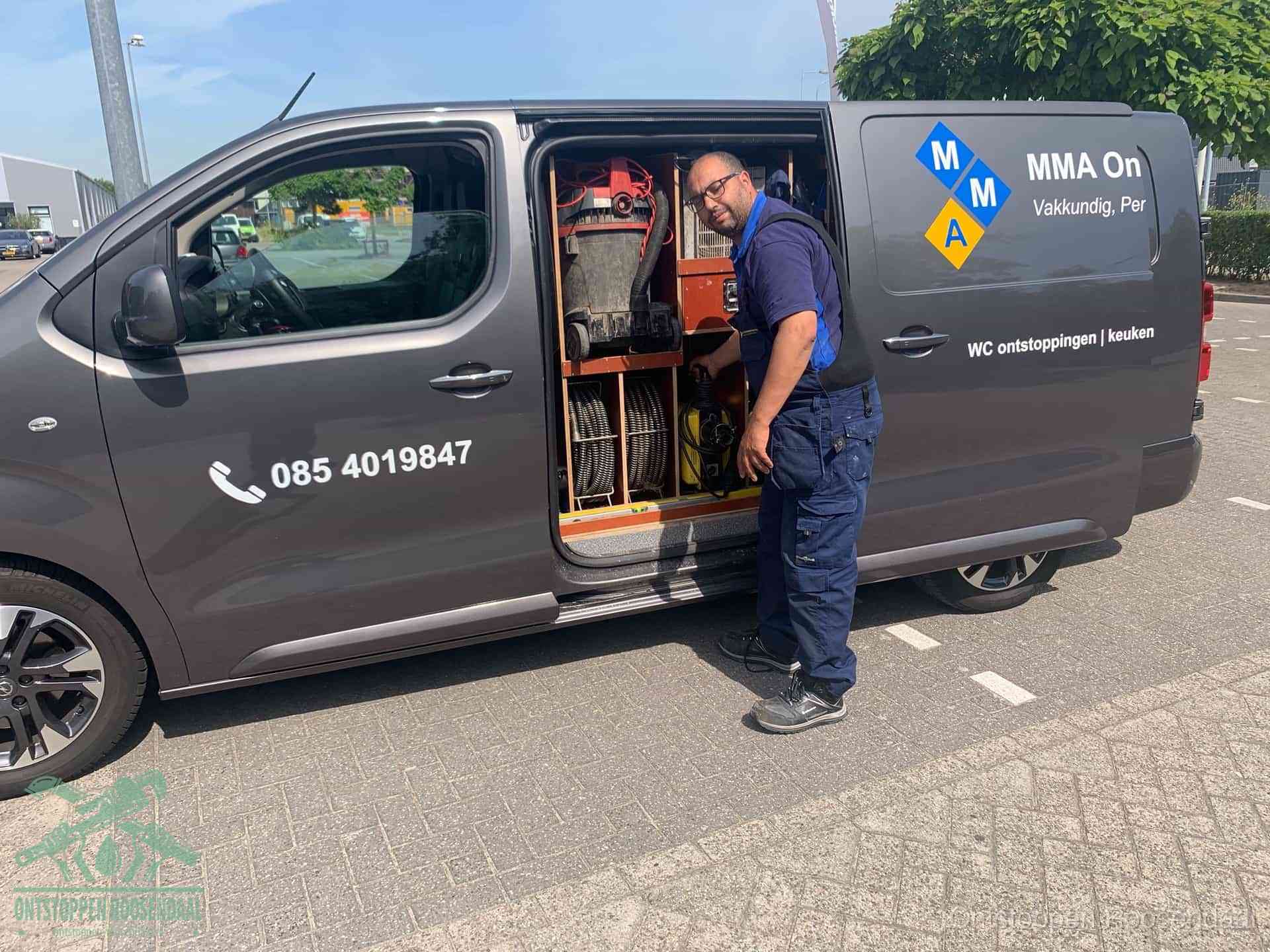 Een monteur bij de open schuifdeur van zijn bedrijfsbus op een parkeerplaats, klaar om de oorzaak van terugkerende afvoerverstoppingen aan te pakken in Roosendaal