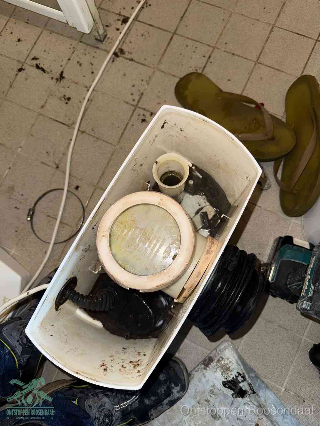 Een gedemonteerde toiletpot op de vloer met ontstoppingsveer en gereedschap ernaast, het verwijderen van een vastzittend voorwerp uit de wc in Roosendaal